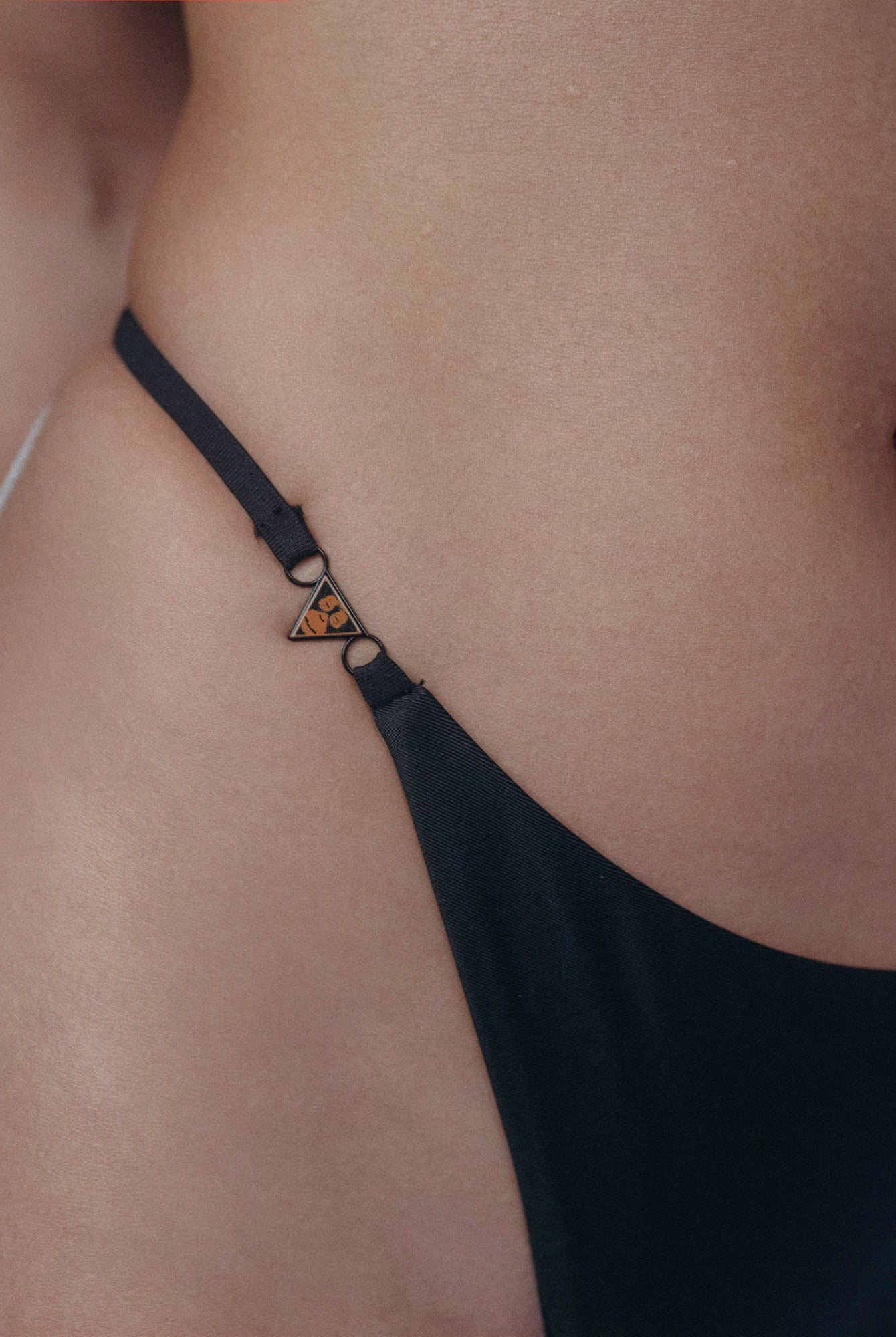 This image features the Sakari Bikini bottom in black, with a close up of the Ohrangatang clasp. The design includes intricate detailing such as a low-rise silhouette that enhances its stylish appeal.