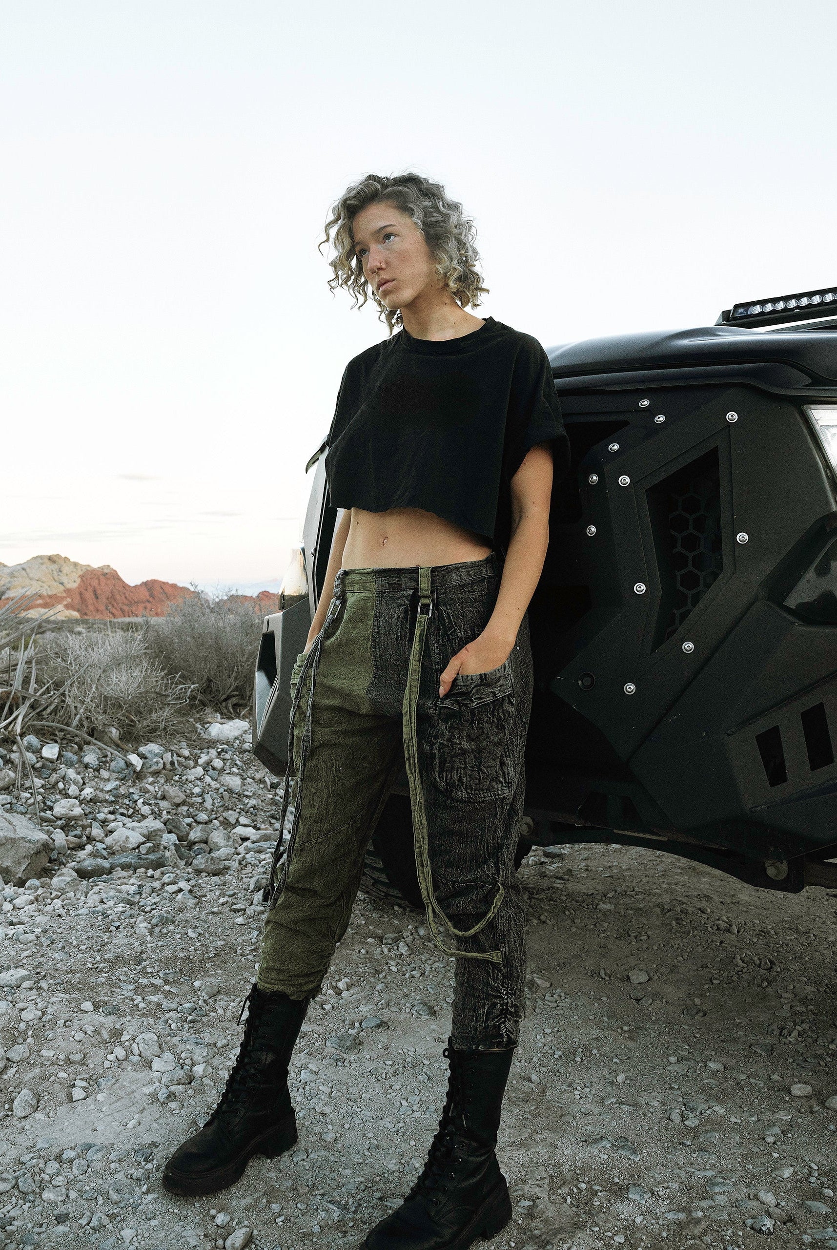 Person wearing the Berghain pants standing in a desert with a black vehicle in the background.