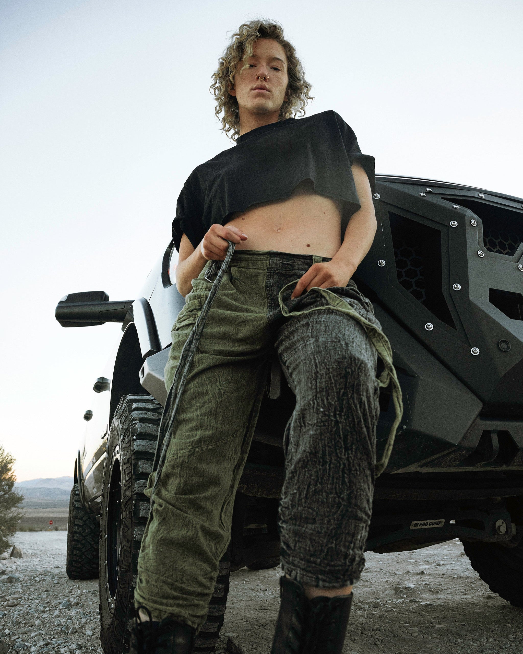 Person wearing the Berghain pants standing in a desert with a black vehicle in the background.