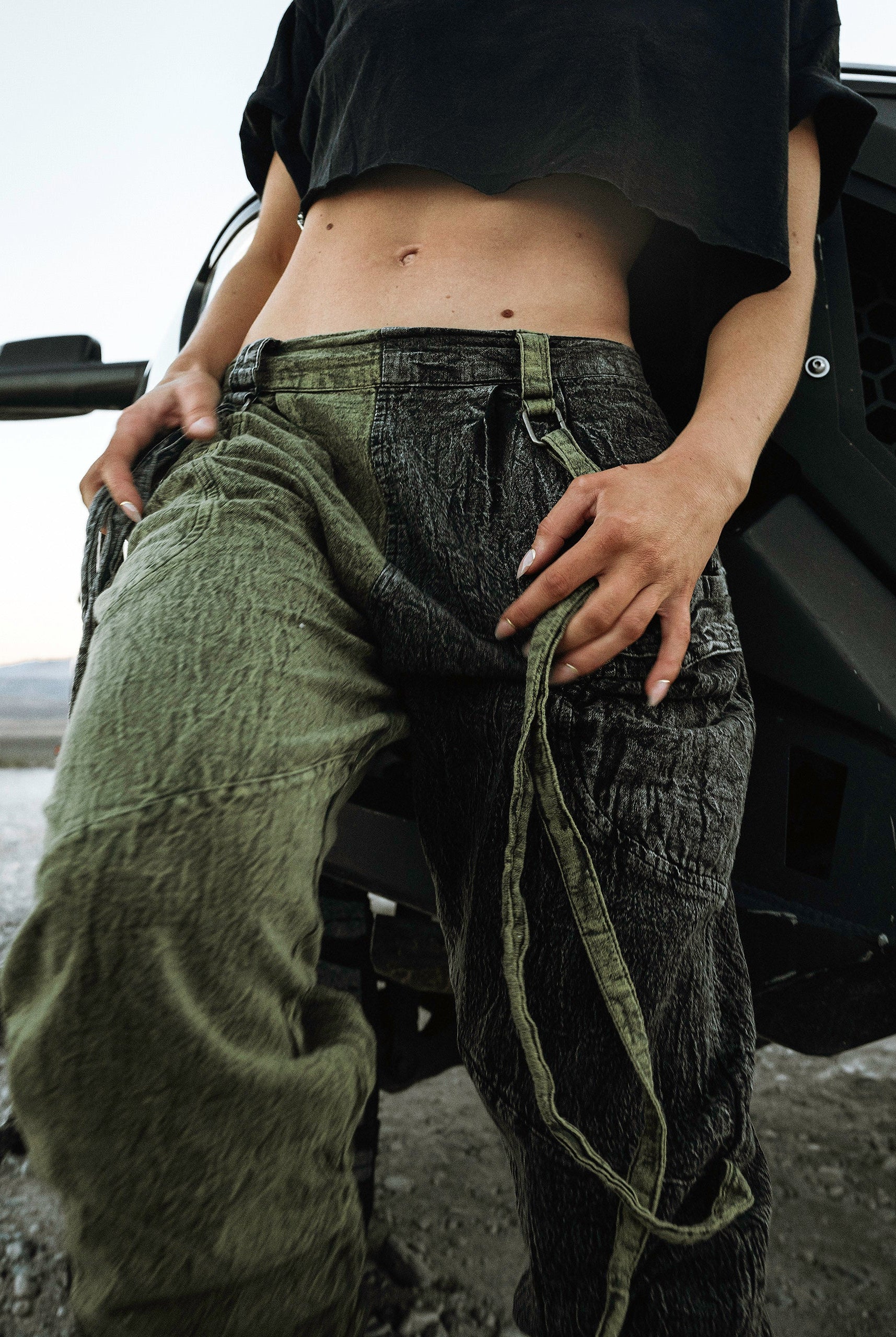 Person wearing the Berghain pants standing in a desert with a black vehicle in the background.