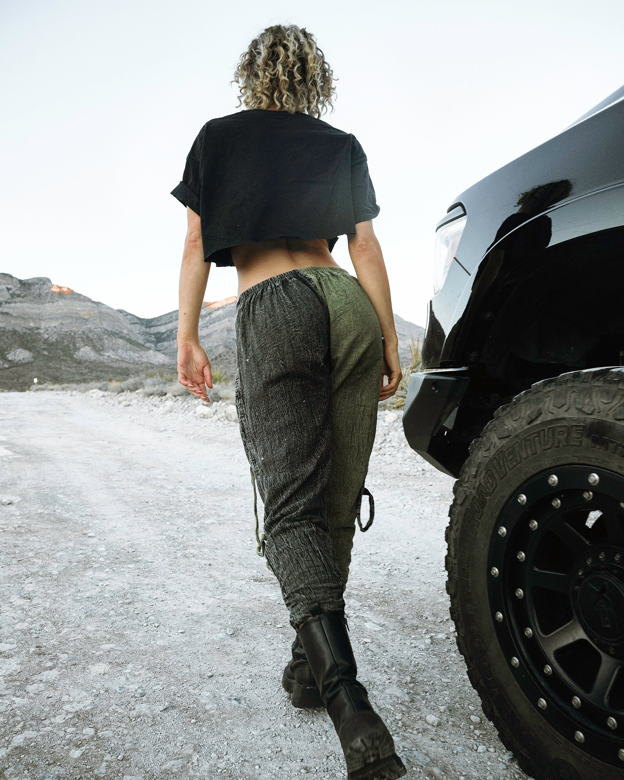 Person wearing the Berghain pants standing in a desert with a black vehicle in the background.