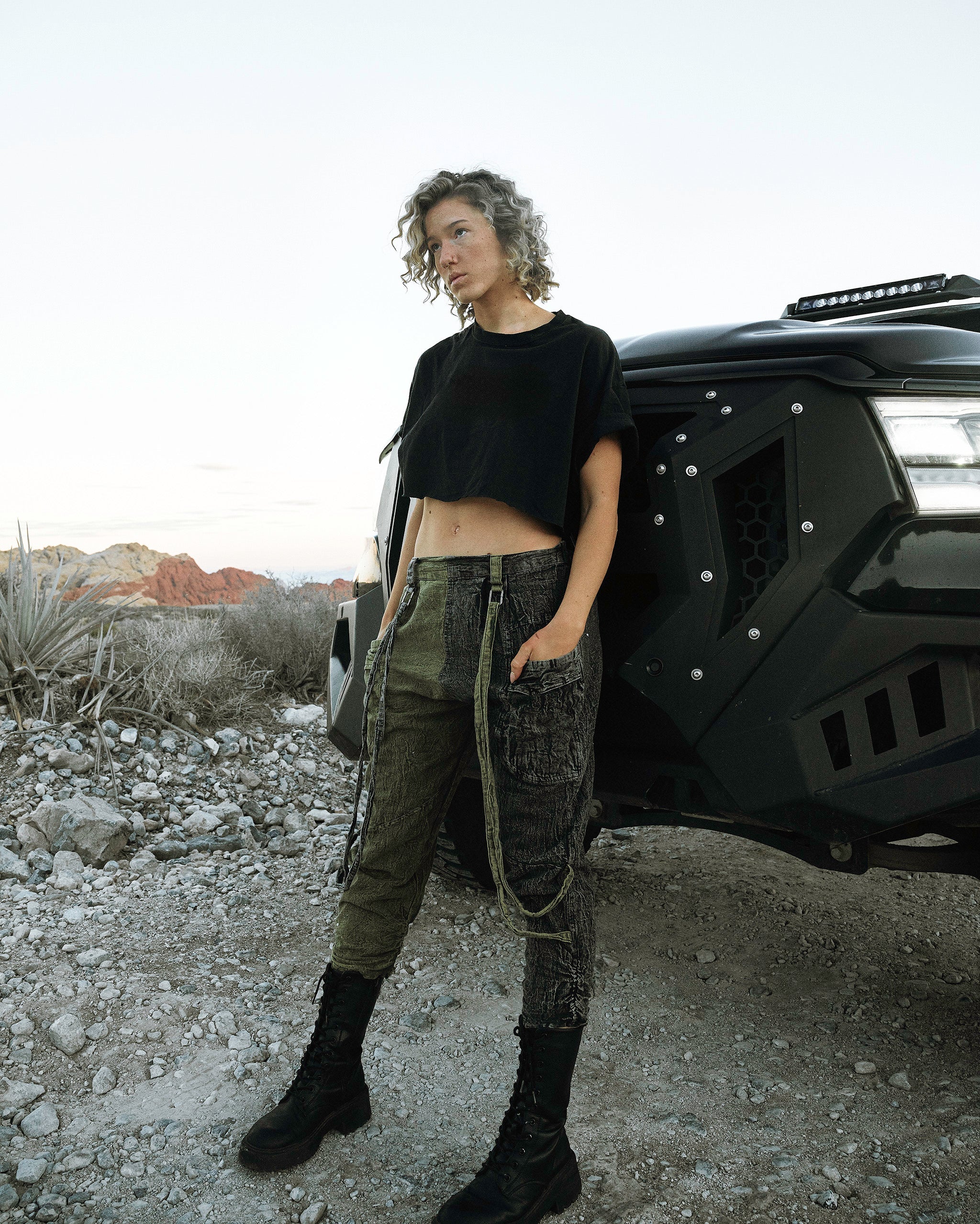 Person wearing the Berghain pants standing in a desert with a black vehicle in the background.