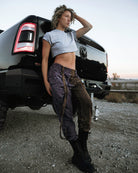 Person wearing the Berghain pants standing in a desert with a black vehicle in the background.